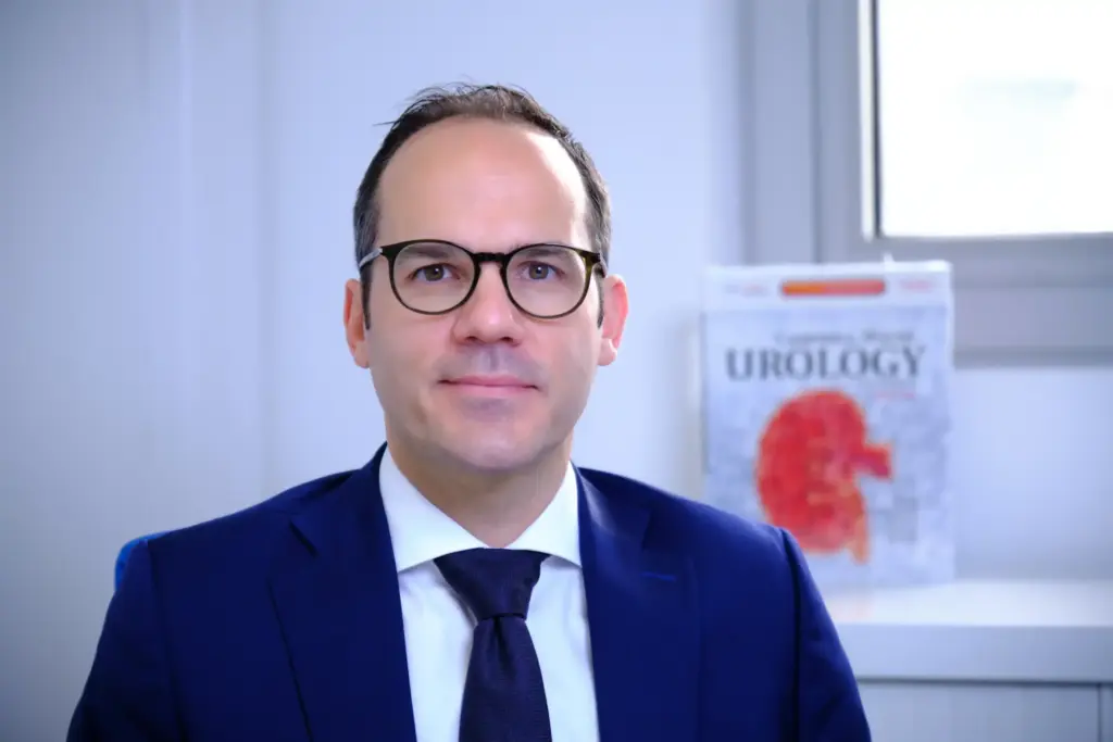 Prof. F.-X. Madec à son bureau rédigeant une publication scientifique sur les sténoses de l’urètre, avec des ouvrages de référence en urologie, illustrant son expertise dans les cas complexes et récidivants